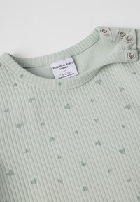 Vaaleanvihreä ribattua vauvan paitaa, jossa on pieniä sydänkuvioita, napit olkapäällä ja koon tarra, jossa lukee 1.5-2 vuotta Ruotsin brändiltä.