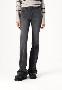 Gray flared jeans with a high waist, featuring subtle stitching and a smooth texture, paired with chunky black platform shoes.