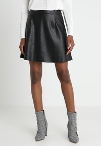 Gonna a forma A in pelle nera con texture liscia, caratterizzata da una vita aderente e un orlo svasato. Abbinata a stivaletti alla caviglia grigio a quadri.