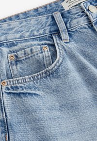 Kirkaste sinise denimbüütsiga teksapüksid, millel on viie tasku disain, vasktooni riistvaraga ja kontrastsete õmblustega õmbluste ääres.