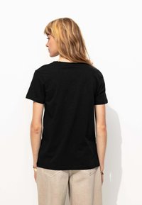 T-shirt en coton noir avec des manches courtes et un col rond. Design simple sans motifs visibles ni accents supplémentaires.