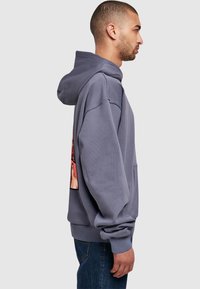 Gray cotton hoodie featuring a kangaroo pocket, oversized fit, and graphic print on the back. Ribbed cuffs and hem add texture.