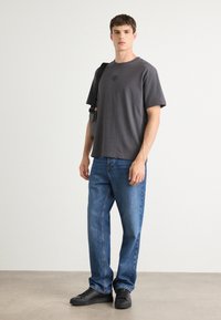 T-shirt en coton gris avec un col rond et un logo, associée à un jean en denim bleu et des baskets noires, sur un fond neutre.