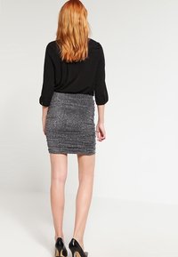 Blouse noire à manches retroussées associée à une mini-jupe argentée métallisée, cintrée et froncée, mise en valeur par des chaussures noires à talons hauts.