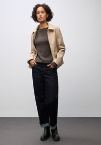 Beige Wollmischjacke mit einem Hemdkragen, getragen über einem dunkelbraunen Pullover und dunklen Jeans, ergänzt durch schwarze Stiefeletten.