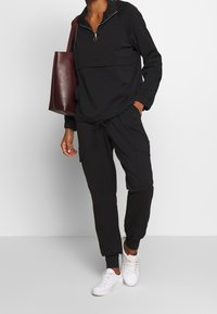 Czarna rozpinana pulower z kieszenią kangurzą, w połączeniu z pasującymi spodniami cargo, które mają regulowany sznurek i boczne kieszenie.