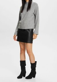 Harmaa ribattupaita yhdistetty mustaan nahkainen minihameeseen ja polvipitkiin mustiin daimikenkiin, joissa on paksu korko.