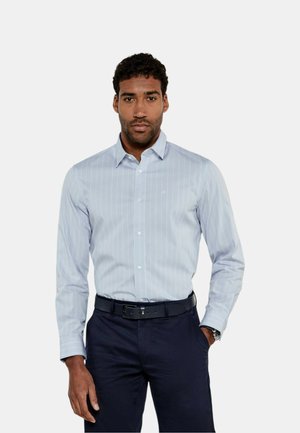 Camicia a righe blu chiaro con colletto button-down, maniche lunghe e vestibilità slim, abbinata a pantaloni scuri e una cintura nera.