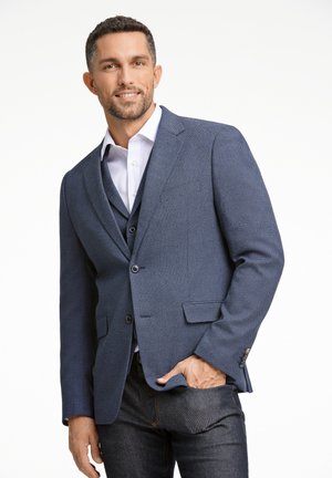 Blazer texturizzato blu navy con due bottoni, tasche laterali e revers a punta, indossato sopra una camicia bianca e jeans in denim.