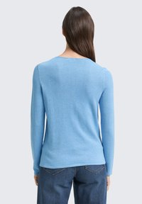Hellblaue, langärmlige Pullover mit rundem Halsausschnitt, aus weichem Strickstoff. Getragen mit dunkelblauen Jeans, die eine glatte Textur zeigen.