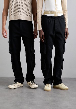 Pantaloni cargo neri con tasche laterali, abbinati a un maglione leggero e a una camicia a maniche lunghe attillata. Le calzature includono sneakers con punte e sneakers classiche.