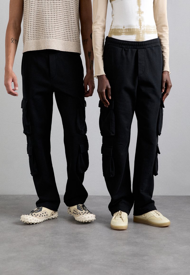 Pantaloni cargo neri con tasche laterali, abbinati a un maglione leggero e a una camicia a maniche lunghe attillata. Le calzature includono sneakers con punte e sneakers classiche.