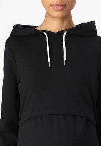 Black maternity hoodie with a cropped design, featuring a front kangaroo pocket, white drawstrings, and a soft textured fabric.