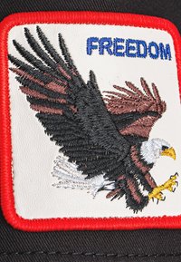 Casquette en tissu noir avec une patch rectangulaire blanche portant un aigle brodé détaillé et le mot "LIBERTÉ" en bleu, entouré de rouge.