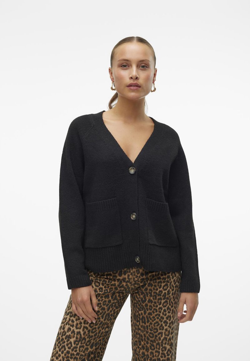 Gilet noir à col en V, avec des boutons sur le devant, des bords côtelés et deux poches avant. Texture douce, coupe décontractée, associé à un pantalon imprimé léopard.