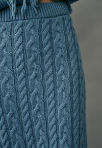 Fustă din tricot cu model de cablu în nuanță de albastru moale. Are un brau ribat și modele intricate de cablu pe întreaga suprafață. Textură moale și croială strâmtă.