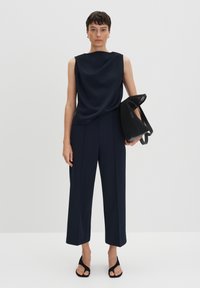 Navy sleeveless top with a draped design paired with wide-leg navy trousers. The model holds a black mesh handbag and wears black heeled sandals.