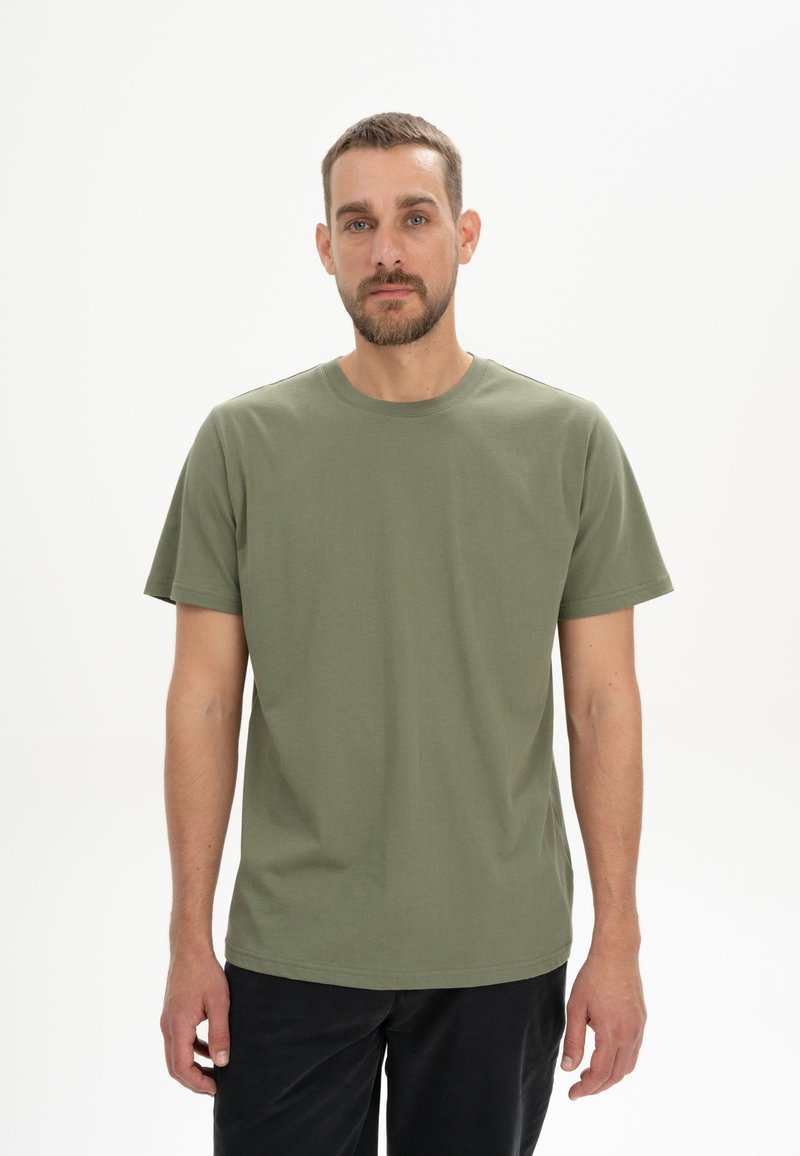 Olivengrünes Baumwoll-T-Shirt mit kurzen Ärmeln und Rundhalsausschnitt, getragen von einem Modell in einer neutralen Umgebung. Einfaches Design ohne Muster.