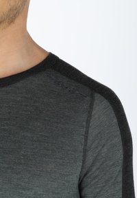 Dark gray long-sleeve shirt with a textured black shoulder panel, ribbed neckline, and subtle branding near the shoulder seam.
