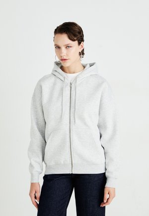 Ljust grå zip-up hoodie i mjukt tyg, med en framficka, ribbade muddar och en rymlig huva. Bärs med mörka jeans.