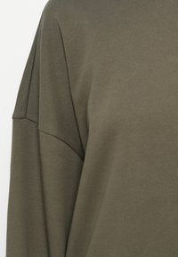 Olive green sweatshirt with a textured fabric. Features dropped shoulder design and a relaxed fit. Simple, minimalistic style.