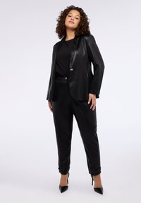 Czarny, dopasowany garnitur z błyszczącą marynarką na dwa guziki, zestawiony z zwężanymi spodniami. Stylizację uzupełniają czarne, szpiczaste szpilki.