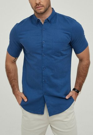 Chemise à manches courtes avec boutonnage en bleu profond, dotée d'une poche poitrine, d'une texture lisse, d'un col structuré et de détails subtils sur les boutons.