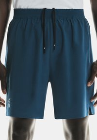 Blue athletic shorts made from soft fabric, featuring an elastic waistband, adjustable drawstring, and side slits for enhanced mobility.