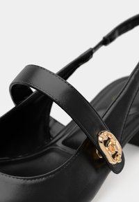 Black patent leather shoe with a slingback design, featuring a decorative gold hardware accent on the strap and a low heel.