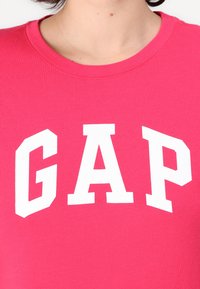 Lyserød bomulds t-shirt med et stort hvidt "GAP" logo i en fed, atletisk skrifttype. Rund halsudskæring med en glat tekstur.