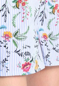 Květinové kraťasy v světlé modré barvě s vertikálními bílými pruhy, zdobené barevnými květinami a zelení, vyrobené z lehkého materiálu.