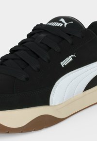 Baskets Puma noires avec bande latérale blanche, lacets noirs, semelle intermédiaire beige et détail de semelle extérieure en caoutchouc marron.