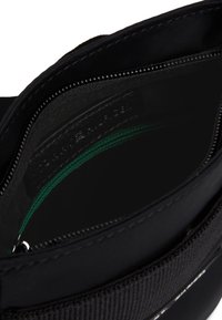 Schwarze Reißverschlusstasche mit einem teilweise geöffneten Hauptfach, das eine grüne Reißverschluss-Tasche und einen Stoffinnenfutter zeigt.