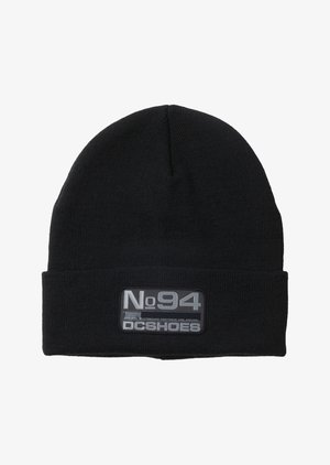 Zwarte gebreide beanie met een omgeslagen rand, voorzien van een rechthoekig grijs patch met "No94 DC Shoes" in het wit gedrukt. Zacht, rekbaar materiaal.