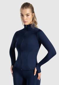 Marinblå zip-up sportjacka tillverkad av slät, elastisk tyg med en figurnära design, hög krage och tumhål på ärmarna.