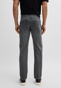 Jeans de mezclilla gris con corte recto, diseño de cinco bolsillos y un parche de marca negro en la cintura. Textura suave con detalles de costura.