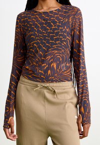 Långärmad skjorta i mörkblått med orange virvlande mönster, tillverkad av ett mjukt tyg, i kombination med beige ribbade sweatpants med snörning.