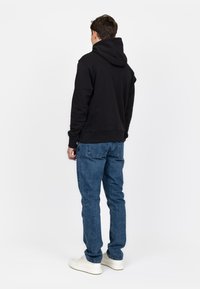 Felpa nera con cappuccio sul retro, abbinata a jeans di denim blu e sneakers bianche, con un fit rilassato e una costruzione semplice.