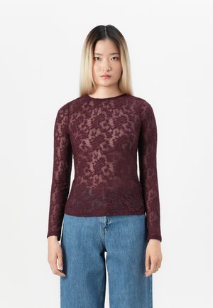 Burgunderrød langermet topp laget av blonde, med blomsterprint, rund hals, og en figurnær passform, kombinert med løse, lyse jeans.