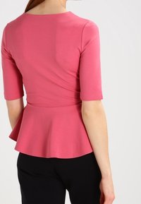 Enganliegender pinker Peplum-Top mit kurzen Ärmeln, runder Halslinie und glatter Textur, kombiniert mit schwarzen Hosen.
