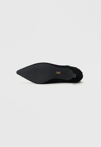 Black suede pointed-toe shoe with a sleek silhouette. Features a smooth sole and a discreet logo accent near the heel.