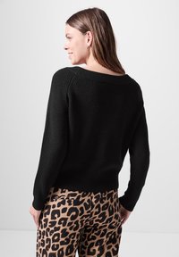 Schwarzer Strickpullover mit weitem Ausschnitt und geripptem Muster, kombiniert mit Leopardenmuster-Hosen mit einer Gesäßtasche.