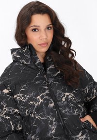 Zwarte en beige marmerpatroon pufferjack met een hoge kraag en ritsluiting, voorzien van een stervormige ritsenhouder en gestructureerde stof.