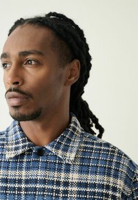 Collared button-up shirt featuring a blue and cream checkered pattern with textured fabric. Close-up view of fabric detail and collar.