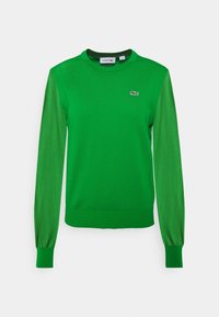 Zielony sweter z pulowerem z długimi rękawami. Posiada okrągły dekolt i prążkowane mankiety. Na piersi znajduje się logo Lacoste w kontrastującym kolorze.