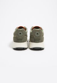 Sneaker verdi in suede con un retro testurizzato, caratterizzati da dettagli in metallo grigio tondo e un interno arancione a contrasto. Suola bianca chunky.
