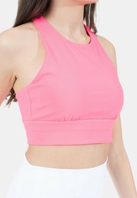 Rosa croppad topp i stretchigt material, med hög halsringning, ärmlös design och samlad fåll för en åtsittande look.