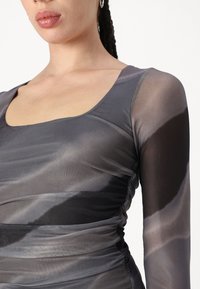 Bluză cu mânecă lungă dintr-un material gri transparent, având un guler rotunjit și detalii pliate pe laterale, creând o formă ajustată.