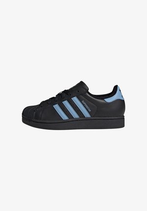 Black leather sneaker featuring three light blue stripes, rubber toe cap, and black laces. The design includes a textured sole and branding.