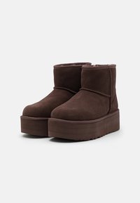 Brown suede ankle boots with a thick, flat platform sole, rounded toe, and soft inner lining. Detailed stitching accents around the upper.